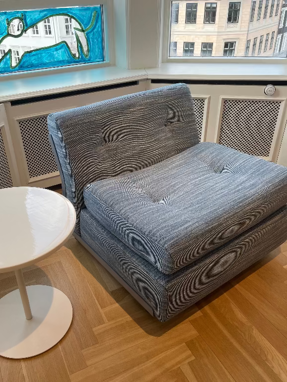 Hay Amanta blue sofa in a room with wooden flooring and a small round table.