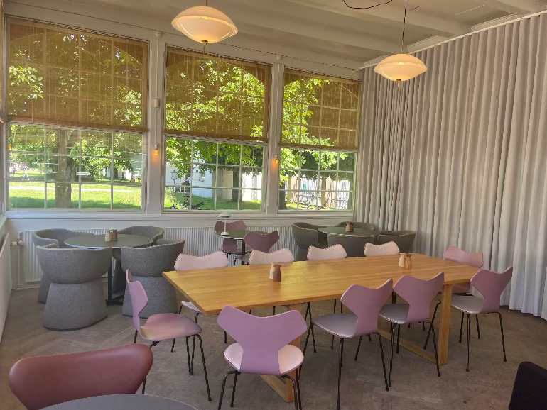 Modern interior with tables and chairs near large windows at the Orangeriet restaurant in Copenhagen during 3DD 2025 with Fritz Hansen furniture and lighting