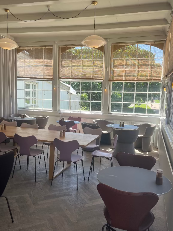 Modern cafe interior with tables and chairs near large windows. Orangeriet in Copenhagen during 3dd 2025 with Fritz Hansen Monolit, Grtand Prix and 3107 chairs. Analogue tables