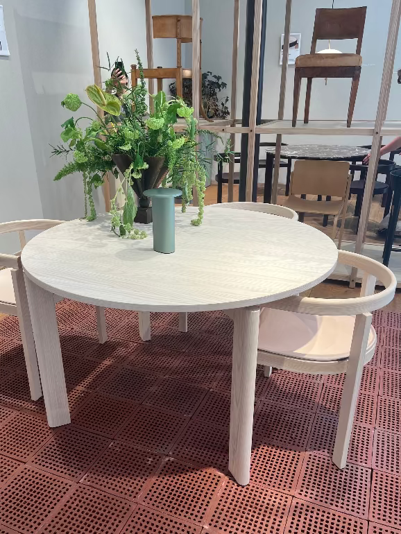 Round white table with chairs and a vase of flowers on a patterned floor. New After dining table and chairs by Michael Anastassiades for Fritz Hansen