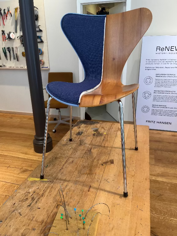 Wooden chair series 7 chair with blue backrest on a wooden floor, with a sign in the background. Fritz Hansen ReNEw programme