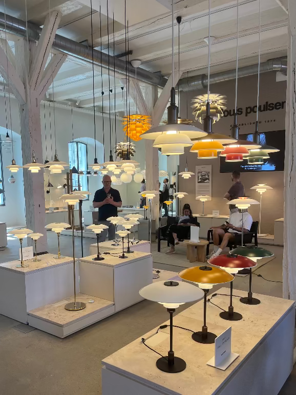 Display of various pendant lights in a showroom setting. Display of modern lamps at a showroom with people observing. Louis Poulsen Copenhagen showroom during 2025 3 Days of Design
