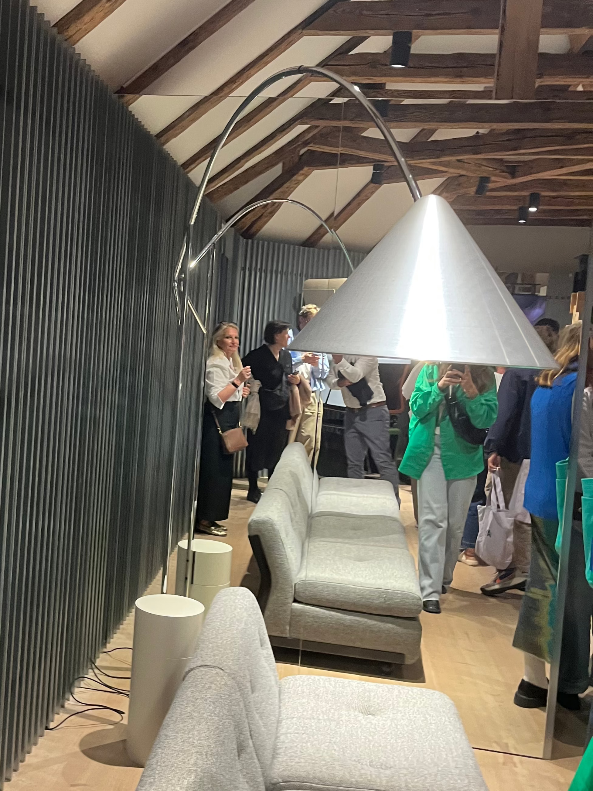 Modern interior design with gray sofas, a large lamp, and people in a showroom setting. concept compass floor lamp for Hay by julien renault - 3dd 2025