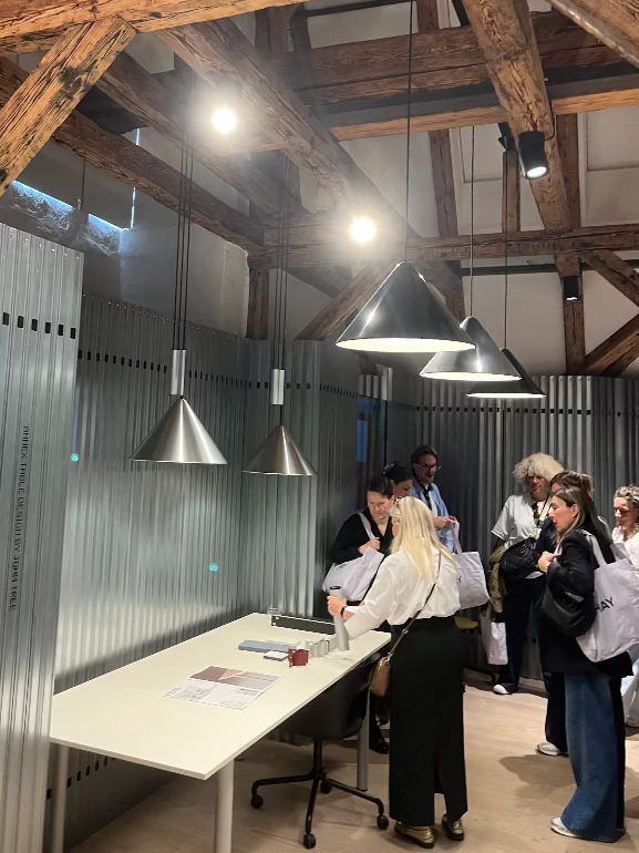 People in a modern office setting with wooden beams and industrial design elements. Hay Compass Pendant launch at 3DD 2025 Copenhagen
