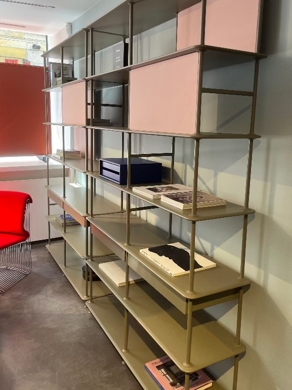 Modern Montana free shelving unit with pink and gold shelves in a room with red chair and concrete floor.