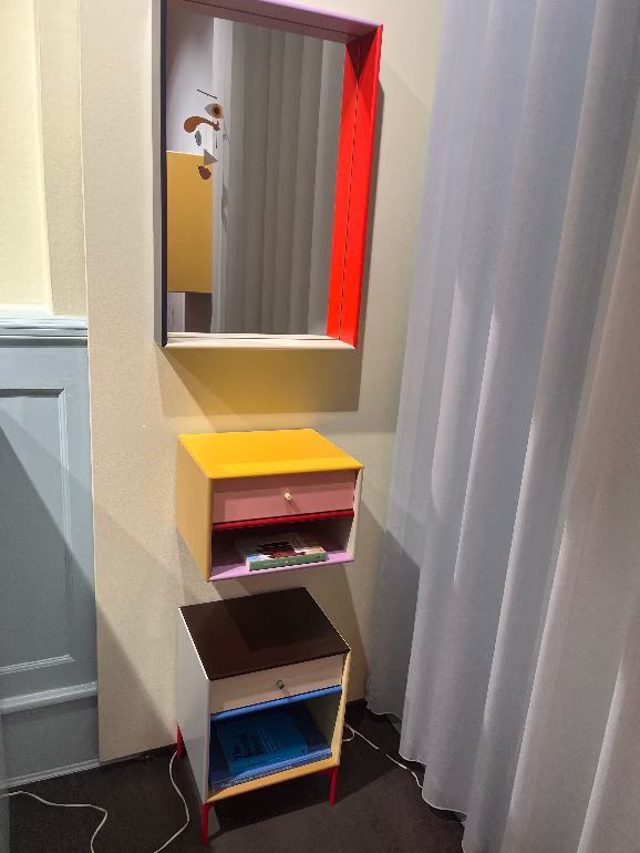 Montana KIMPOP. Small colorful cabinet with a mirror above it next to a white curtain.