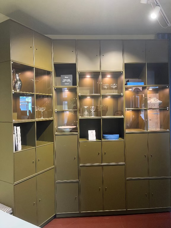 Montana system modular Green storage unit with glass shelves and cabinets in a room setting.