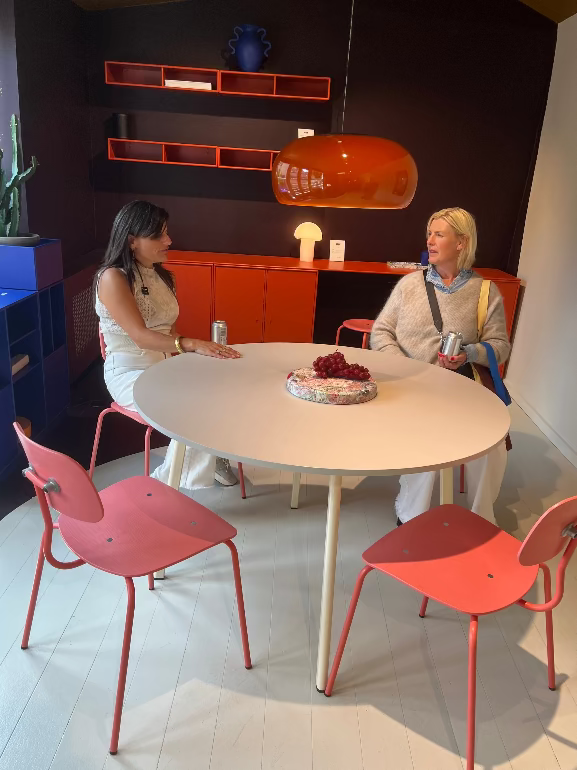 Two women sitting at a round table with pink chairs in a modern interior setting. Montana store copenhagen 3dd 2025. Kevi chair & moser table