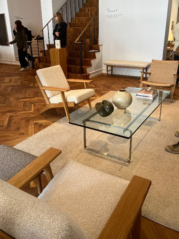 Living room with wooden chairs, glass coffee table, and people in the background. Carl Hansen Copenhagen showroom 3DD 2025. Hans Wegner furniture.