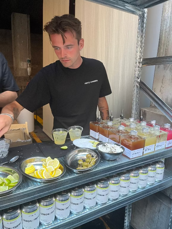Man behind a counter with various drinks and ingredients. Fritz Hansen 2025 party at 3 days of Design at their Copenhagen store.