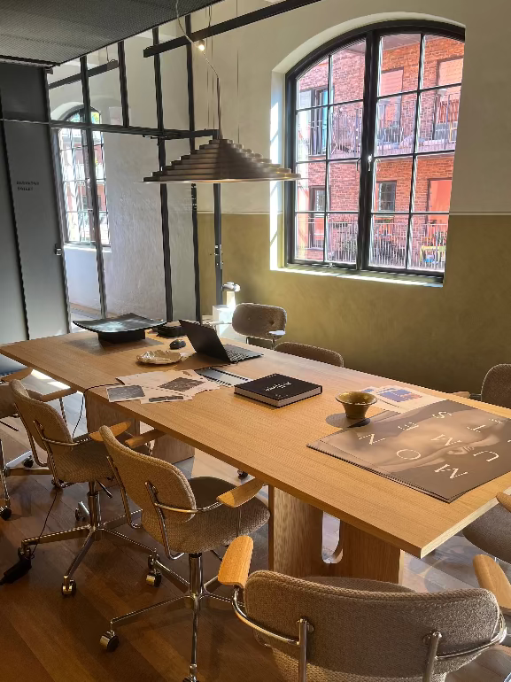 Modern office meeting room with wooden table and chairs, large window in the background. Audo Copenhagen Harbour office chair and new pendant.