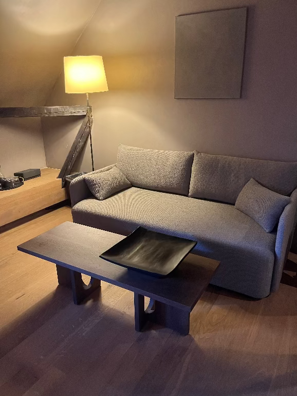 Modern living room with a gray sectional sofa, wooden coffee table, and lamp. Audo Copenhagen Offset Sofa bed
