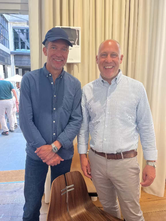 Two men standing next to each other in an indoor setting with a wooden chair and blurred background. David Innes and furniture designer Kasper Saalto at the 3 days of design festival in 2025 Copenhagen at the Fritz Hansen store.