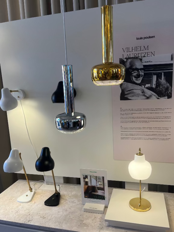 Display of various Vilhelm Lauritzen lamps on a marble surface with a poster in the background at Louis Poulsen's Copenhagen showroom