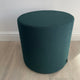 Green cylindrical stool on a wooden floor with a white wall background. Vitra's visiona stool by verner panton in volo green fabric, on display at innes gallery in hessle square, uk