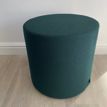 Green cylindrical stool on a wooden floor with a white wall background. Vitra's visiona stool by verner panton in volo green fabric, on display at innes gallery in hessle square, uk