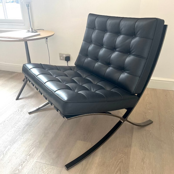 Black leather chair in a room with a desk and wall art. Knoll Barcelona Chair Bauhaus 100th Anniversary Limited Edition Black