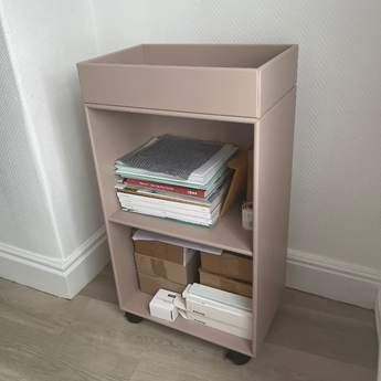 Montana Carry storage wheeled unit. Small beige shelf with books and boxes against a white wall.