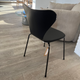 Back of Fritz Hansen 3107 Series 7 Dining chair, front upholstered in black essential leather and black ash frame and black lacquered legs in Innes showroom on oak floor