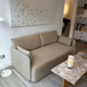 Audo Offset 2 seater sofa in Boucle 02 - A modern beige fabric sofa in a contemporary living room setting, positioned next to a marble-top coffee table with a lit candle, with a large abstract art print on the wall behind it at Innes showroom in Hessle, UK