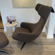 A modern high-back lounge chair upholstered in dark brown fabric with a matching ottoman, shown in a contemporary room with light wood flooring and a small side table. side view of vitra Grand Repos lounge chair with becky innes art print at Innes showroom in Hessle, East Yorkshire
