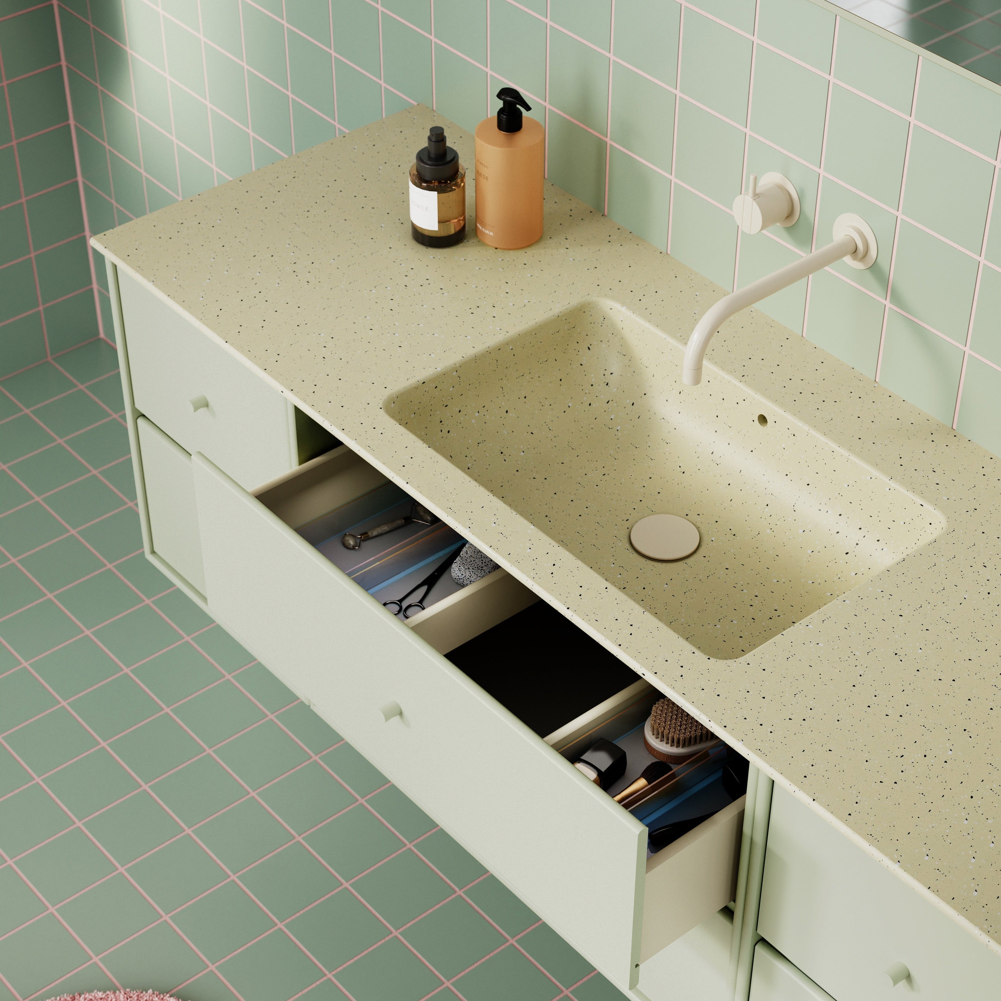 A modern bathroom vanity with a light sage green countertop and sink, set against a matching tiled wall with pink grid lines. The vanity has open drawers showing toiletries inside, and a pink textured rug is visible in the foreground.