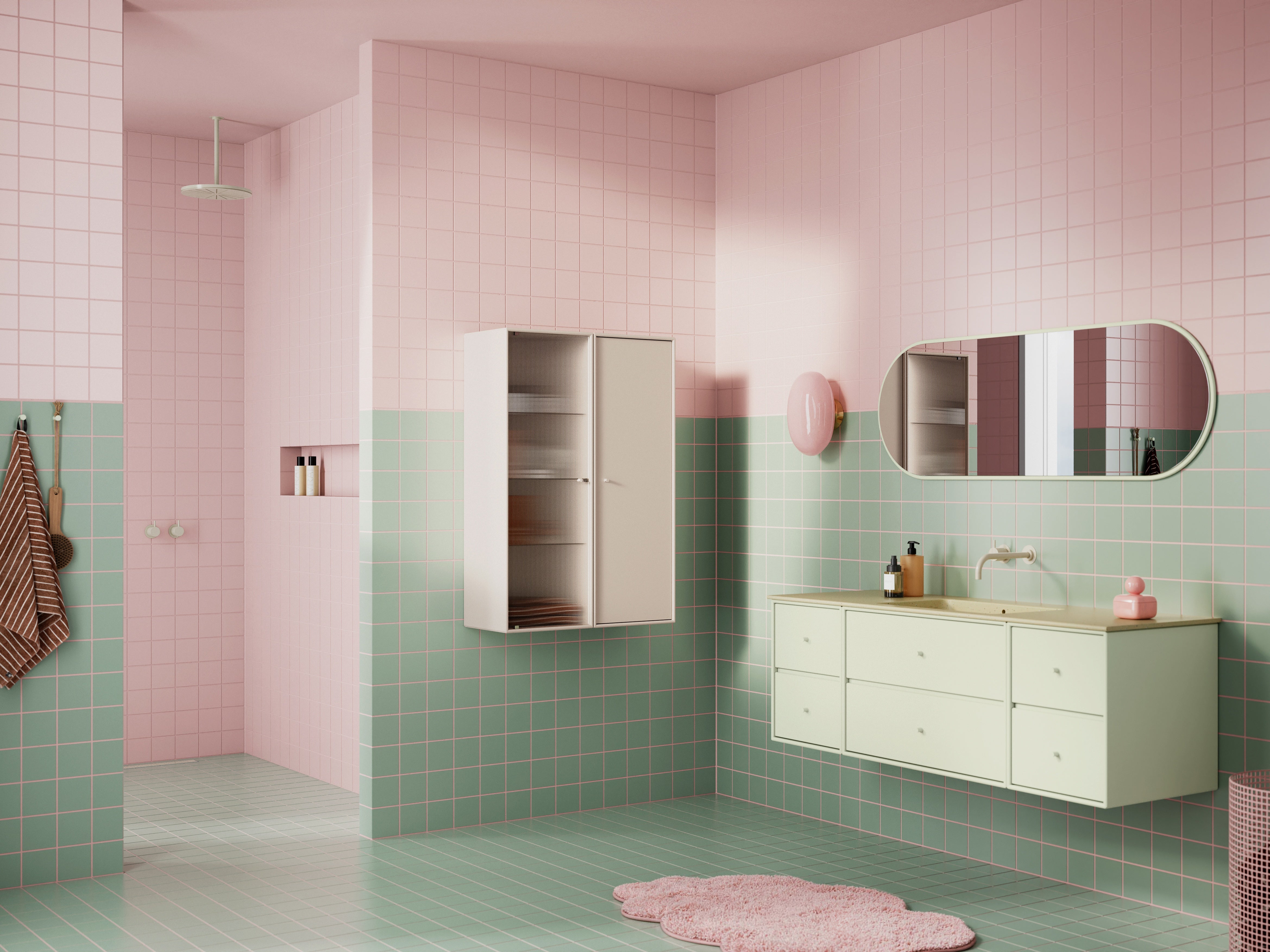 A pastel pink and mint green tiled bathroom interior with a floating vanity, wall-mounted cabinet, oval mirror, shower area, and a pink rug on the floor.