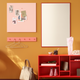 A styled interior scene with a peach square pegboard on a mustard wall, a large white rectangular mirror with a red frame, a red open shelving unit, a beige handbag on the floor, and small decor items on the shelves.