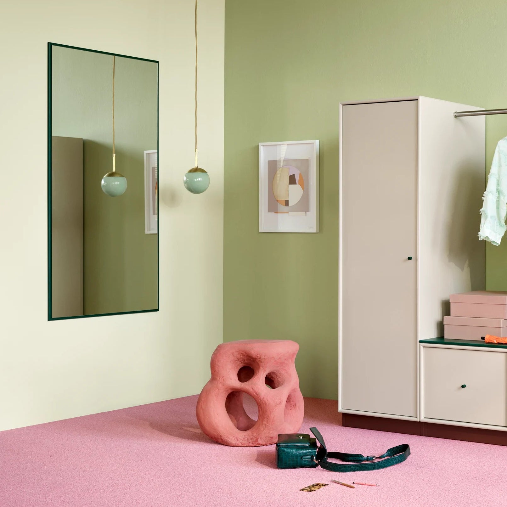 A modern white wardrobe or closet organizer with open shelving and hanging rod, shown in a styled room with a pink floor, sage green walls, a mirror, and a chair.